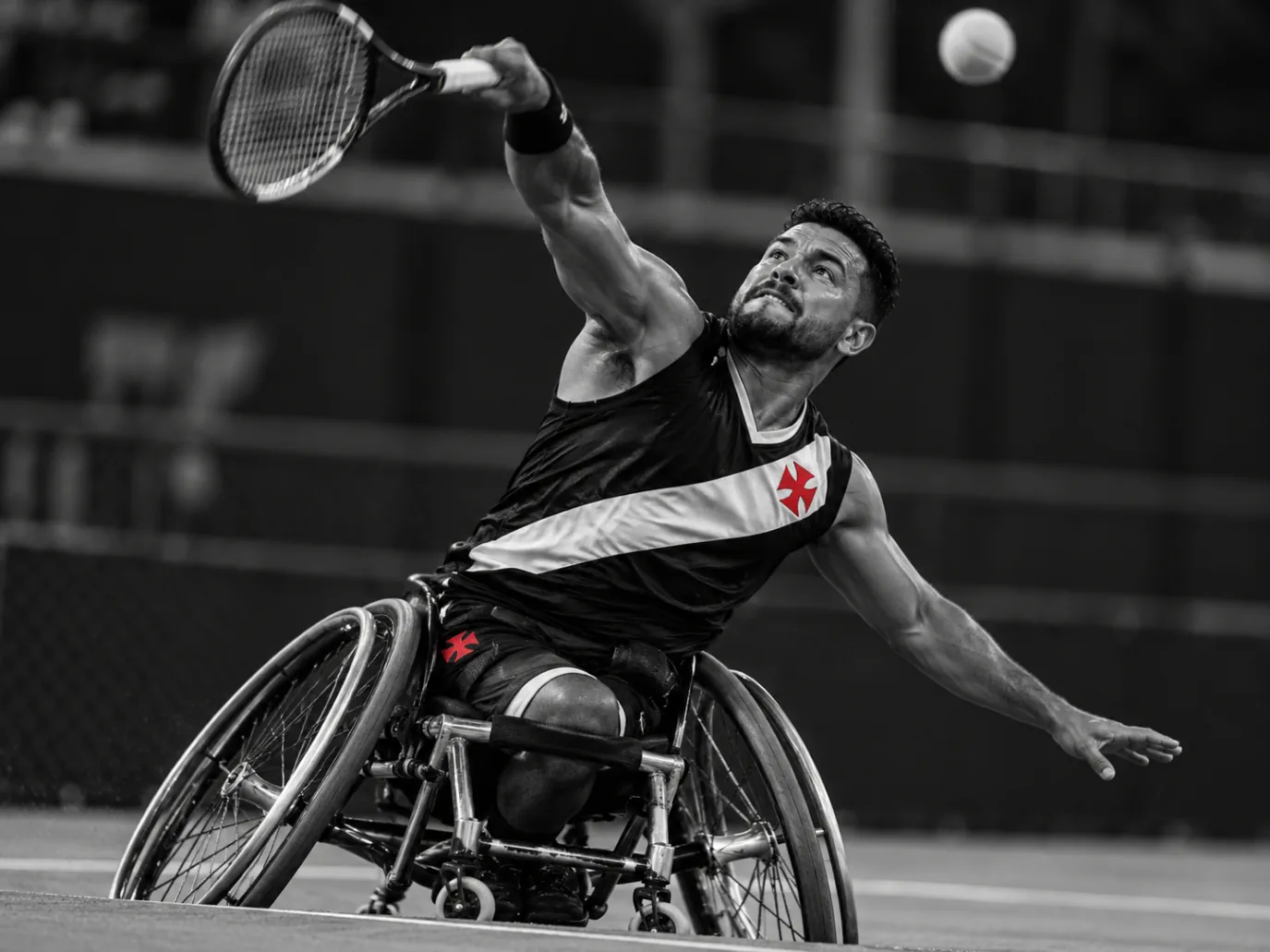 Atleta em cadeira de rodas esportiva estende o braço com a raquete em direção a uma bola alta